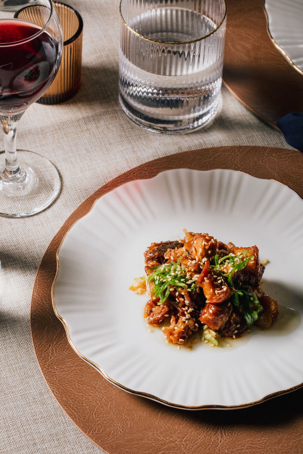 White scalloped plate with glazed broccoli and crispy topping served on a textured brown table setting.