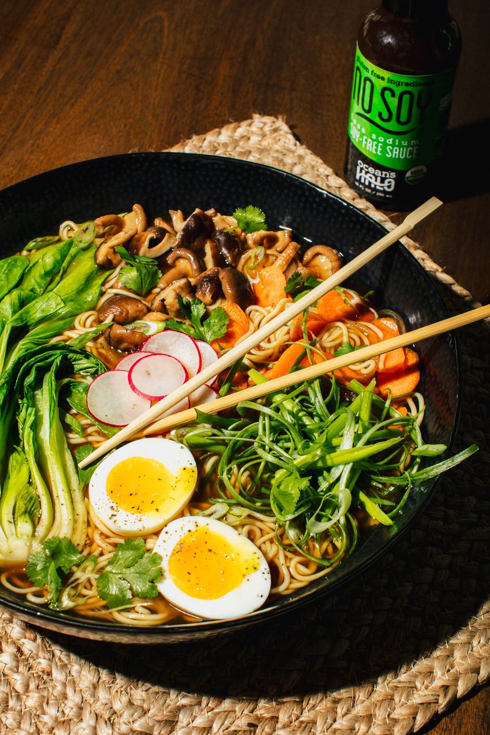 A sequence of ramen noodle bowls with soft boiled eggs, radishes, mushrooms and green vegetables on a dark plate.