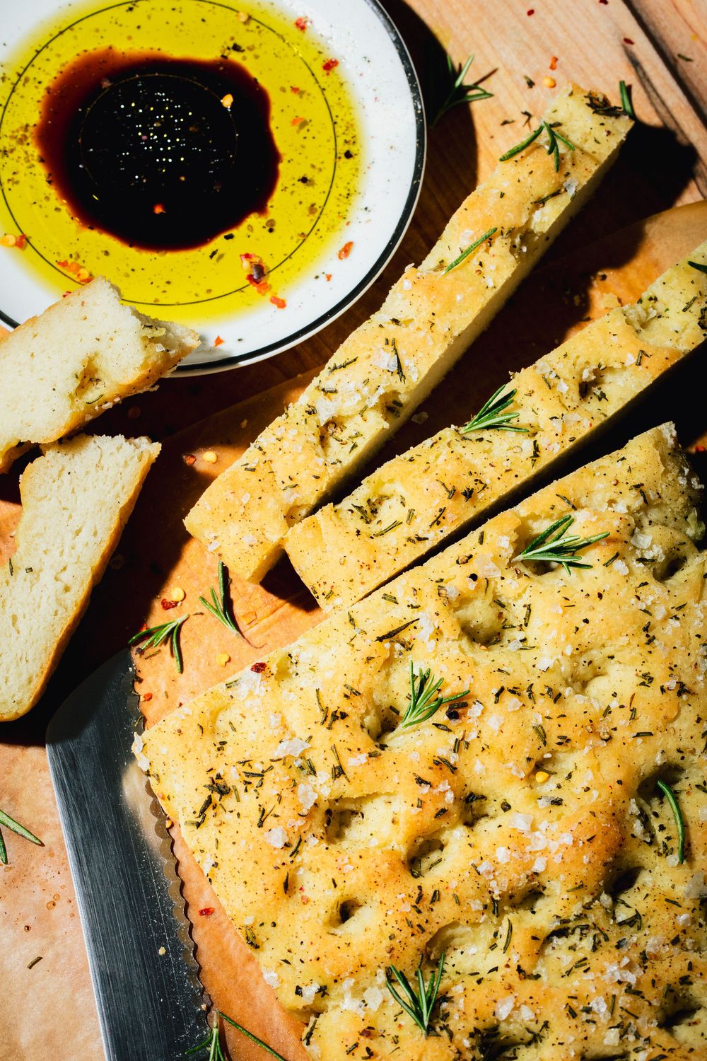 Fresh bread served with olive oil dipping sauce garnished with herbs and spices on a rustic wooden surface.