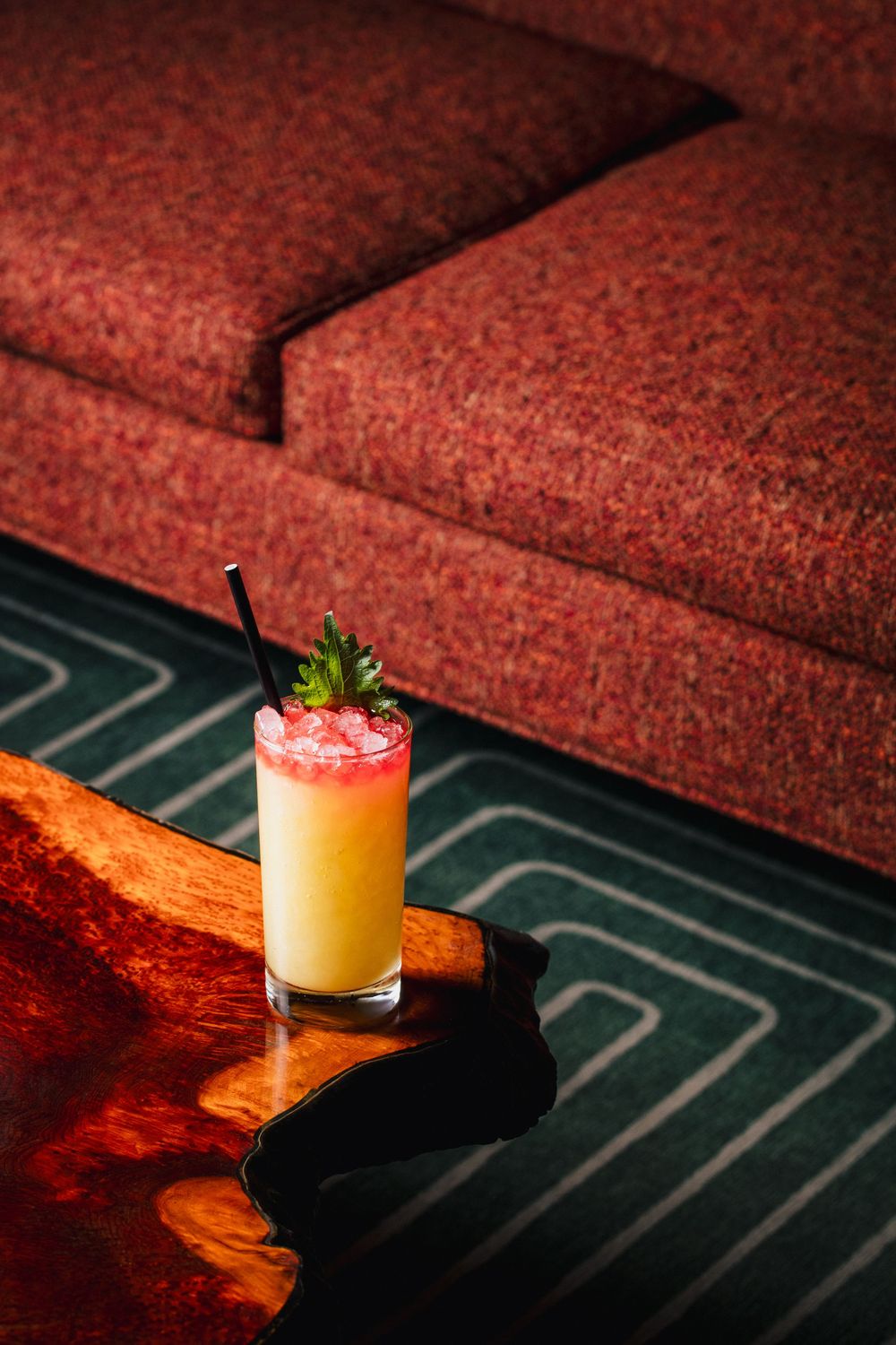 A yellow cocktail with pink salt rim and strawberry garnish is photographed in dramatic lighting on a dark surface.