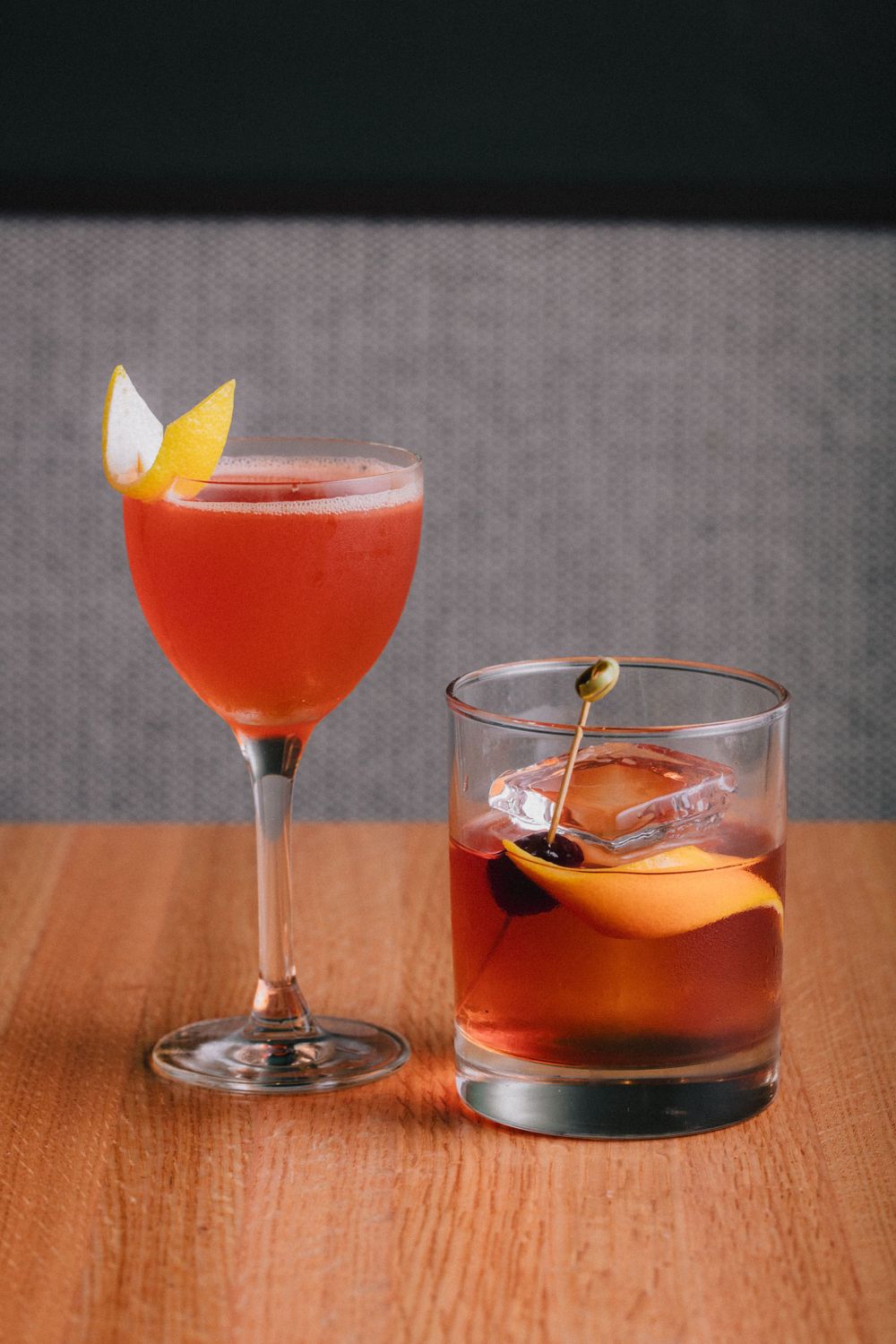 Two elegant cocktails garnished with citrus on wooden table.