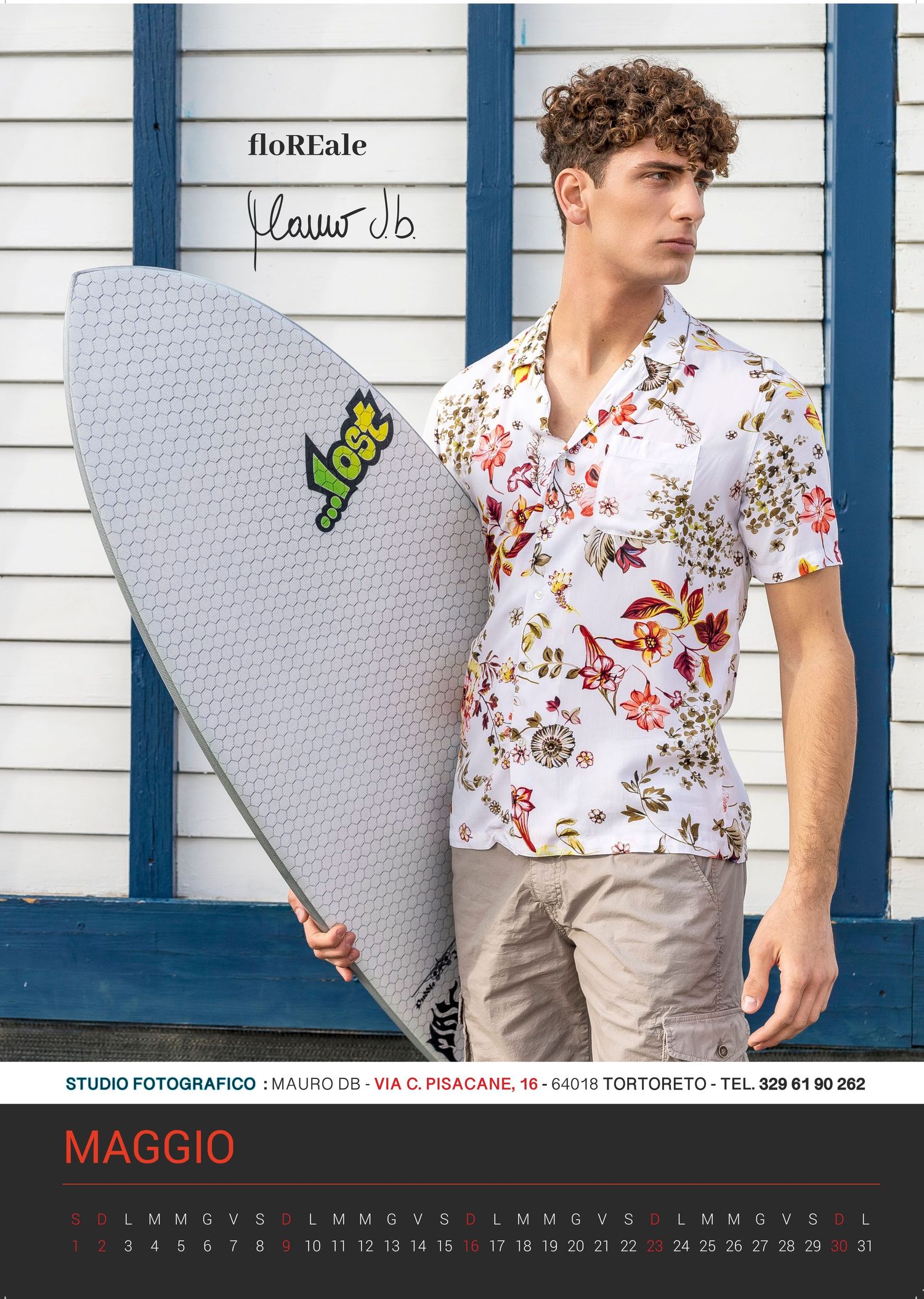 Surfboard leaning against white wall next to model in floral Hawaiian shirt.
