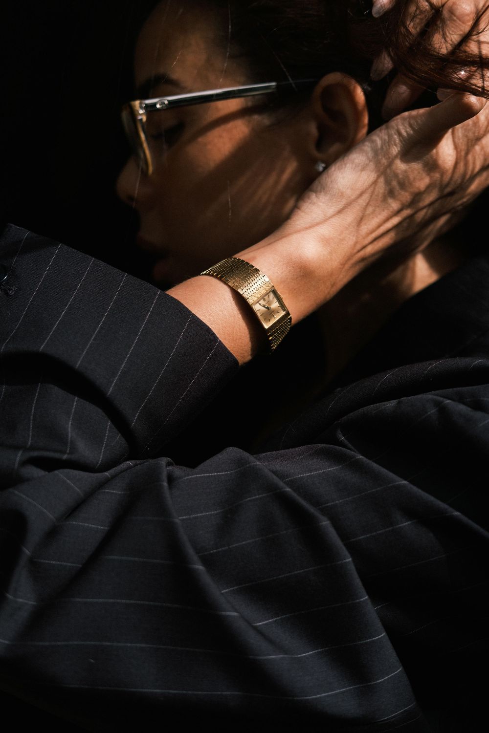 Close-up of a gold watch on a wrist with striped fabric in moody lighting.