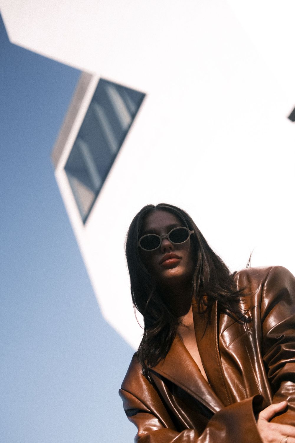 Low angle shot of person in brown leather jacket and sunglasses against blue sky.