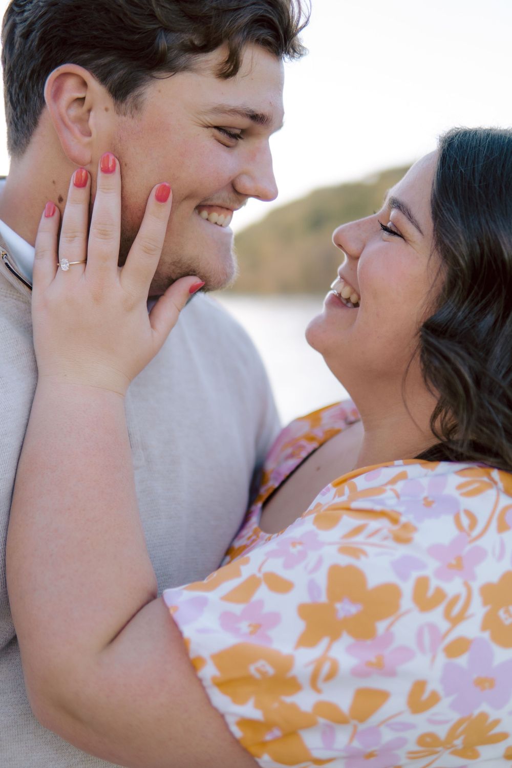 A romantic engagement photo shows a couple embracing outdoors, with the woman displaying her red manicure and ring.