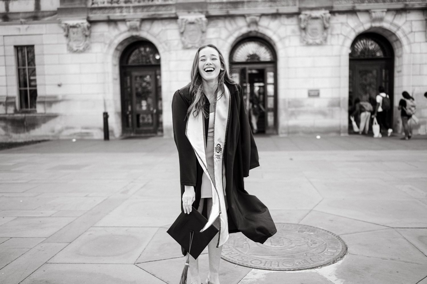 Street style portrait of person in black coat twirling against classical architecture backdrop.