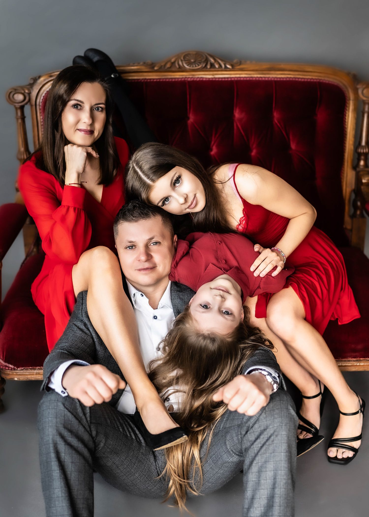 A stylish family portrait on a vintage red velvet couch in coordinating red and black formal attire.