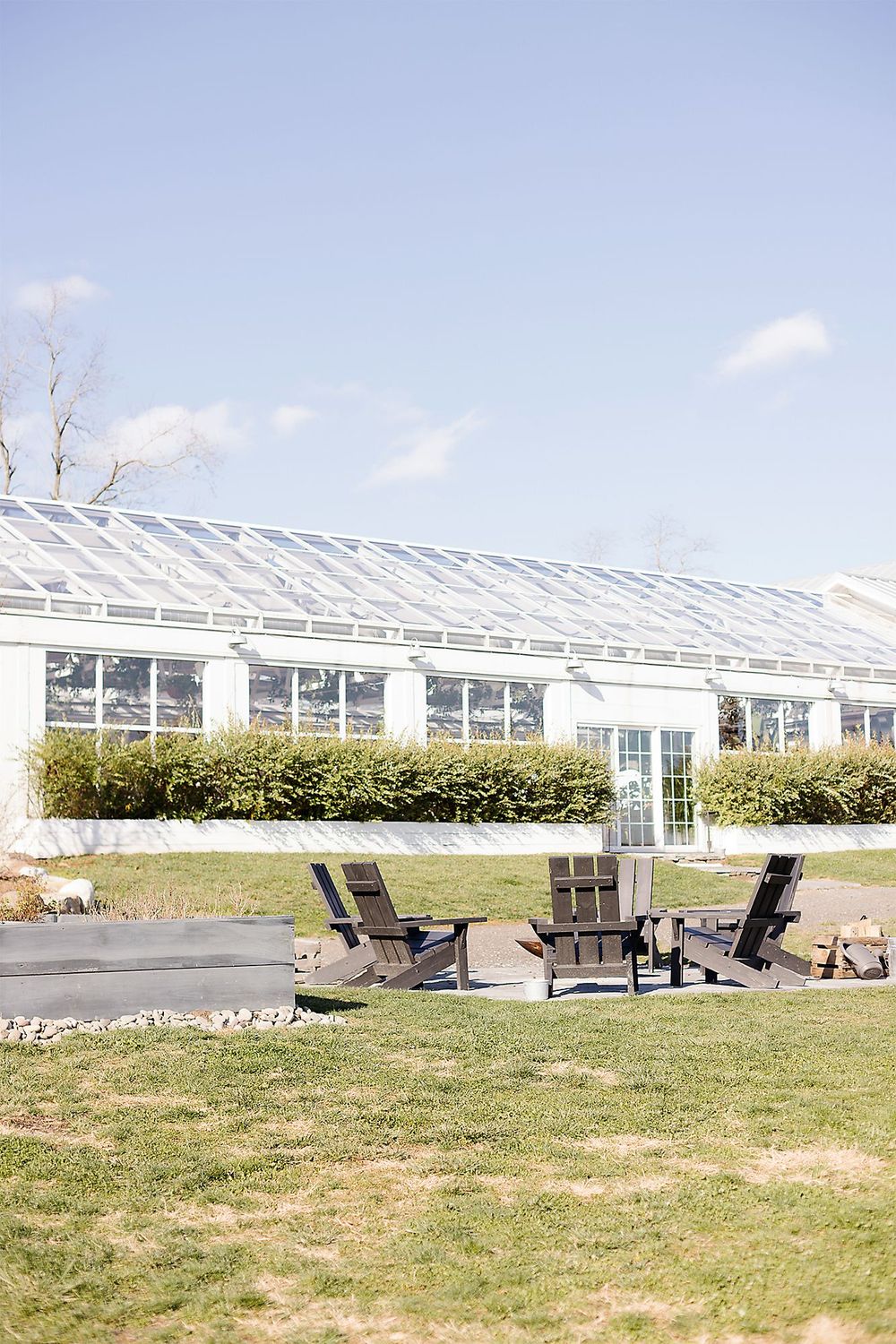 Modern greenhouse exterior with Adirondack chairs on the lawn under blue sky.