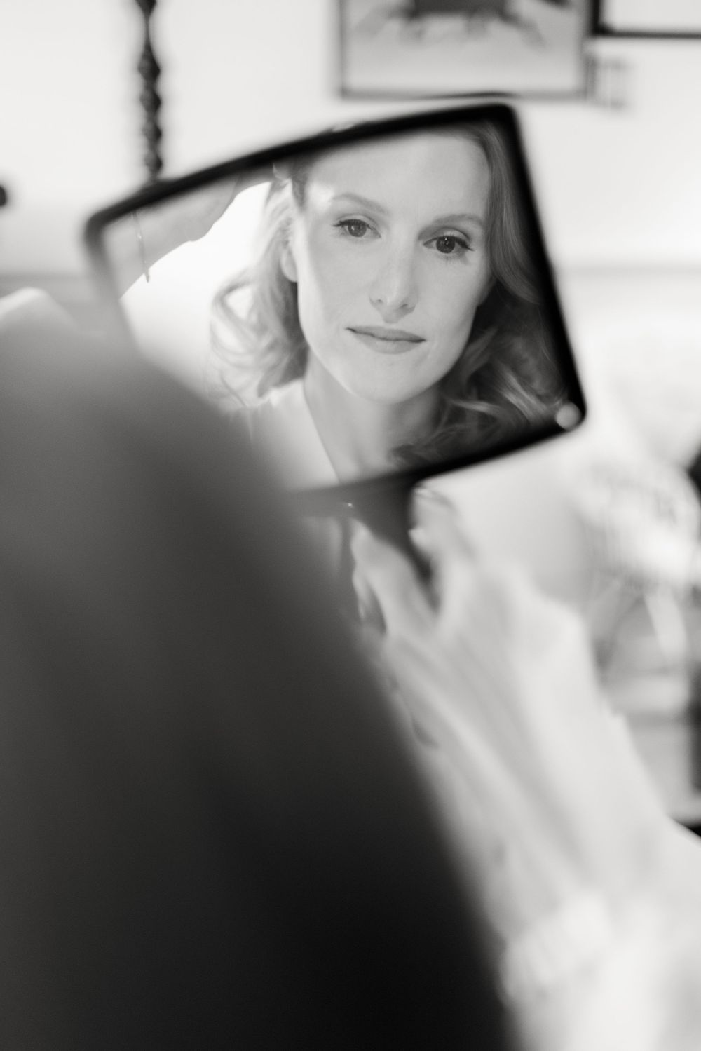 A reflection shows a close-up black and white portrait in a vanity mirror against a soft blurred background.
