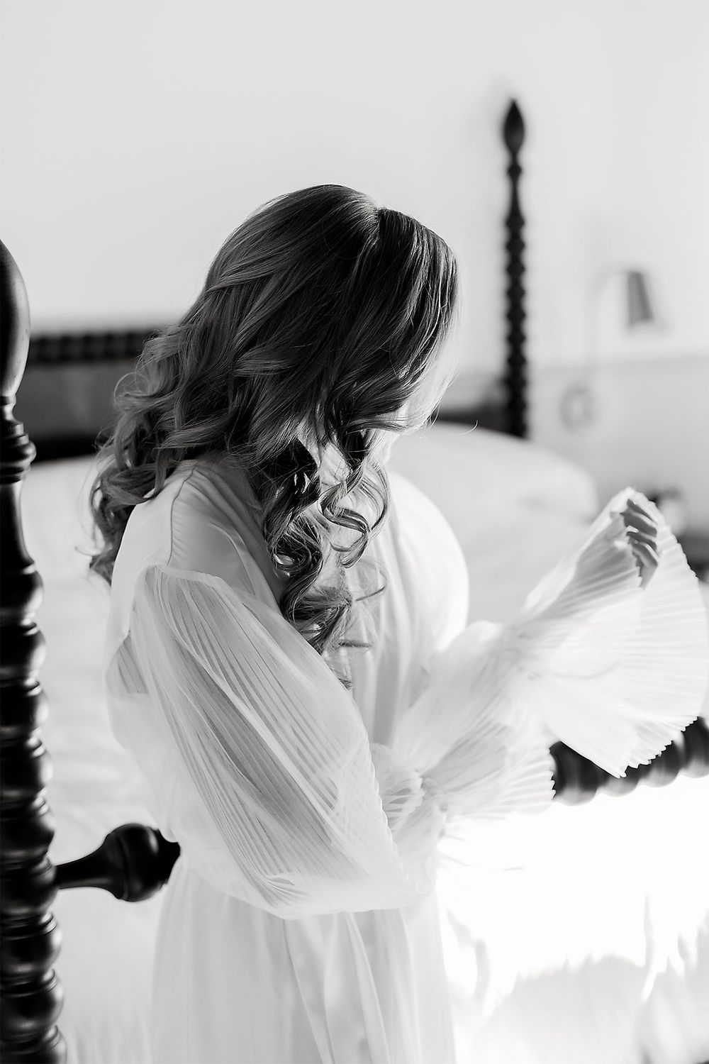 Black and white photo of person in flowing robe getting ready in bedroom with curled hair.