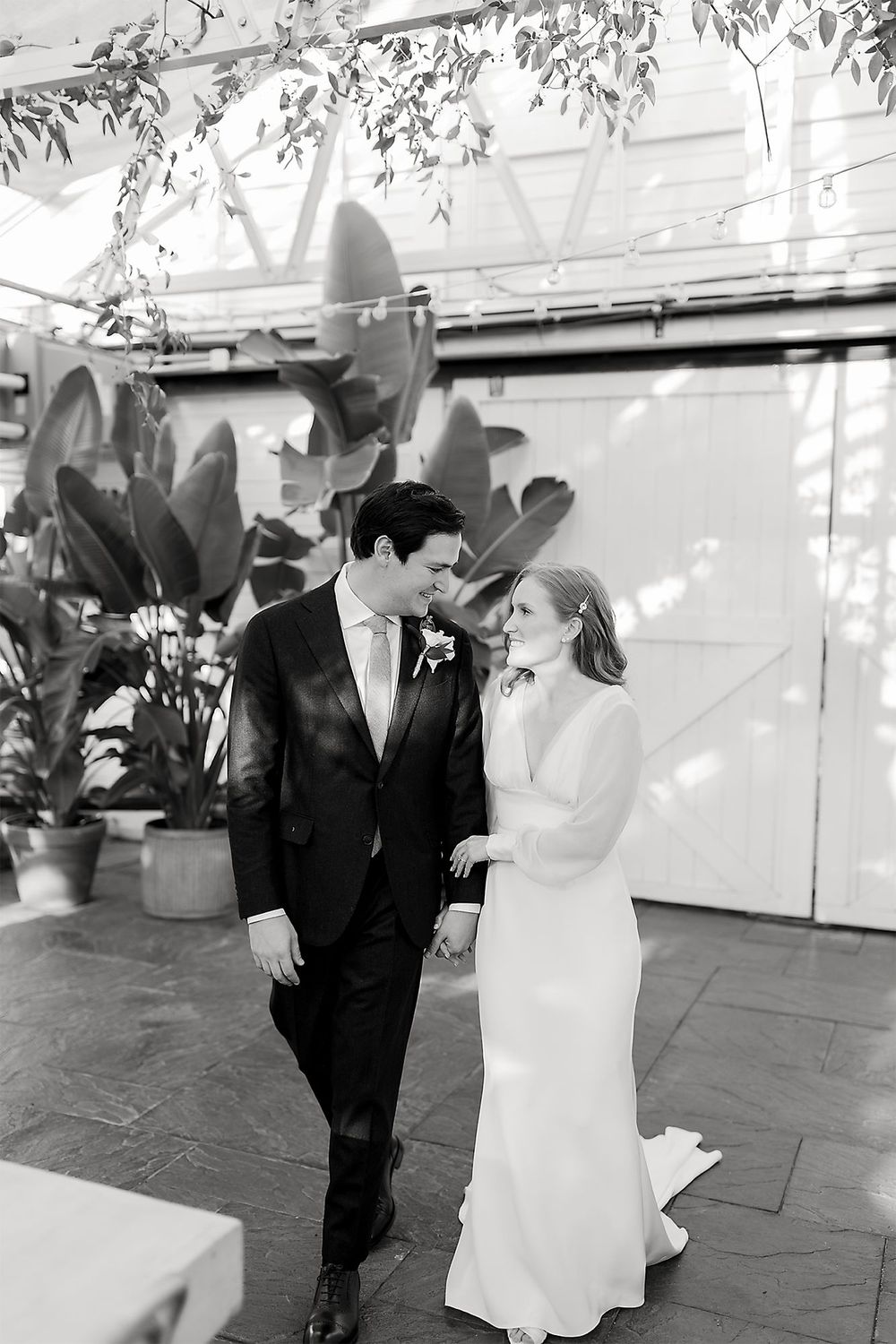 A tender black and white wedding moment captured in a greenhouse setting with greenery and potted plants.
