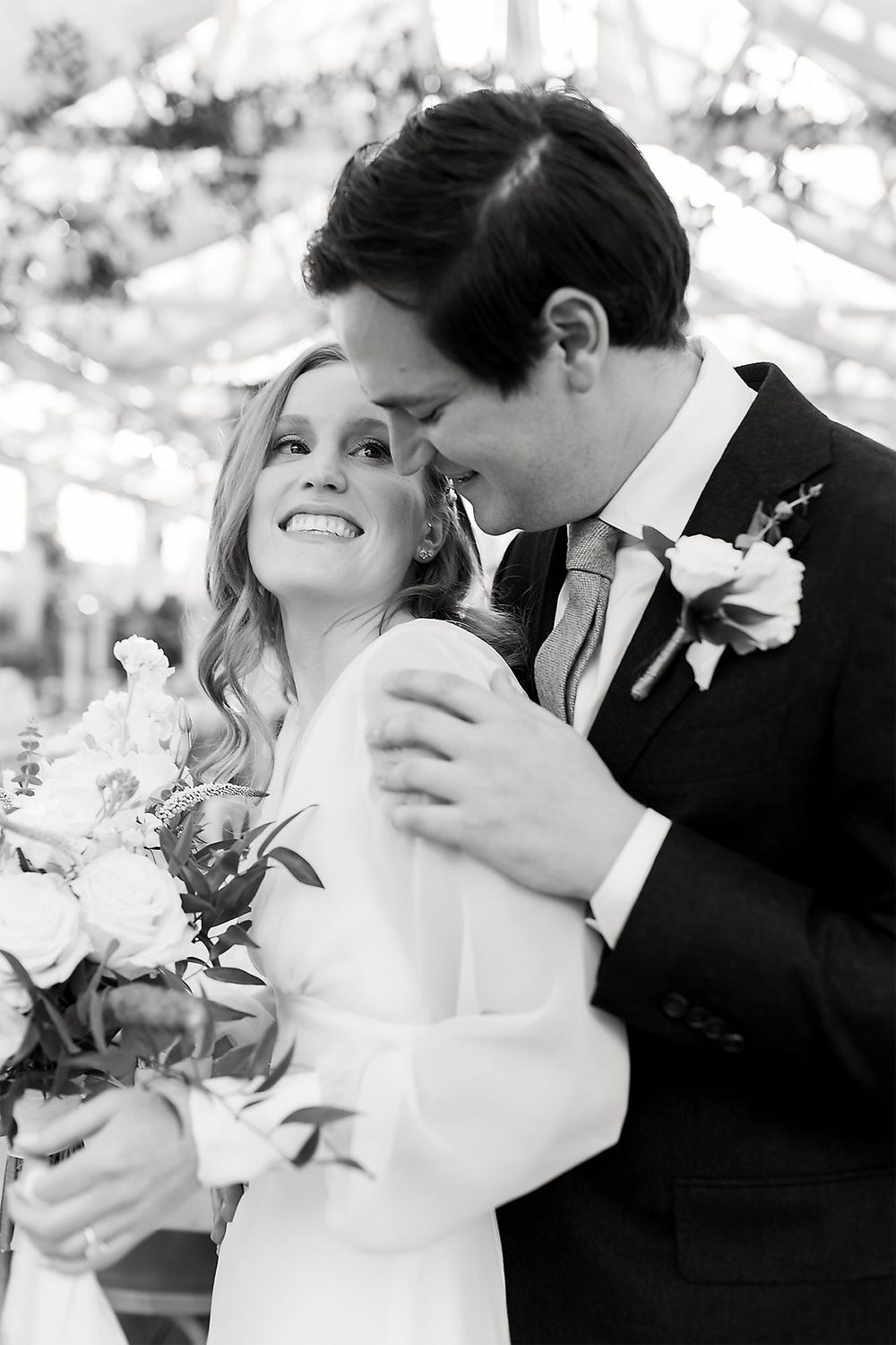 Black and white intimate portrait of newlyweds sharing a joyful moment with bouquet and boutonniere.