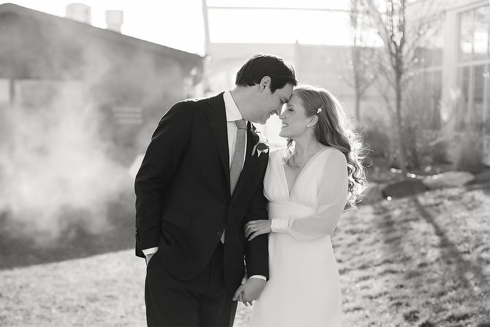 Intimate black and white photo of newlyweds sharing a tender moment in misty outdoor light.