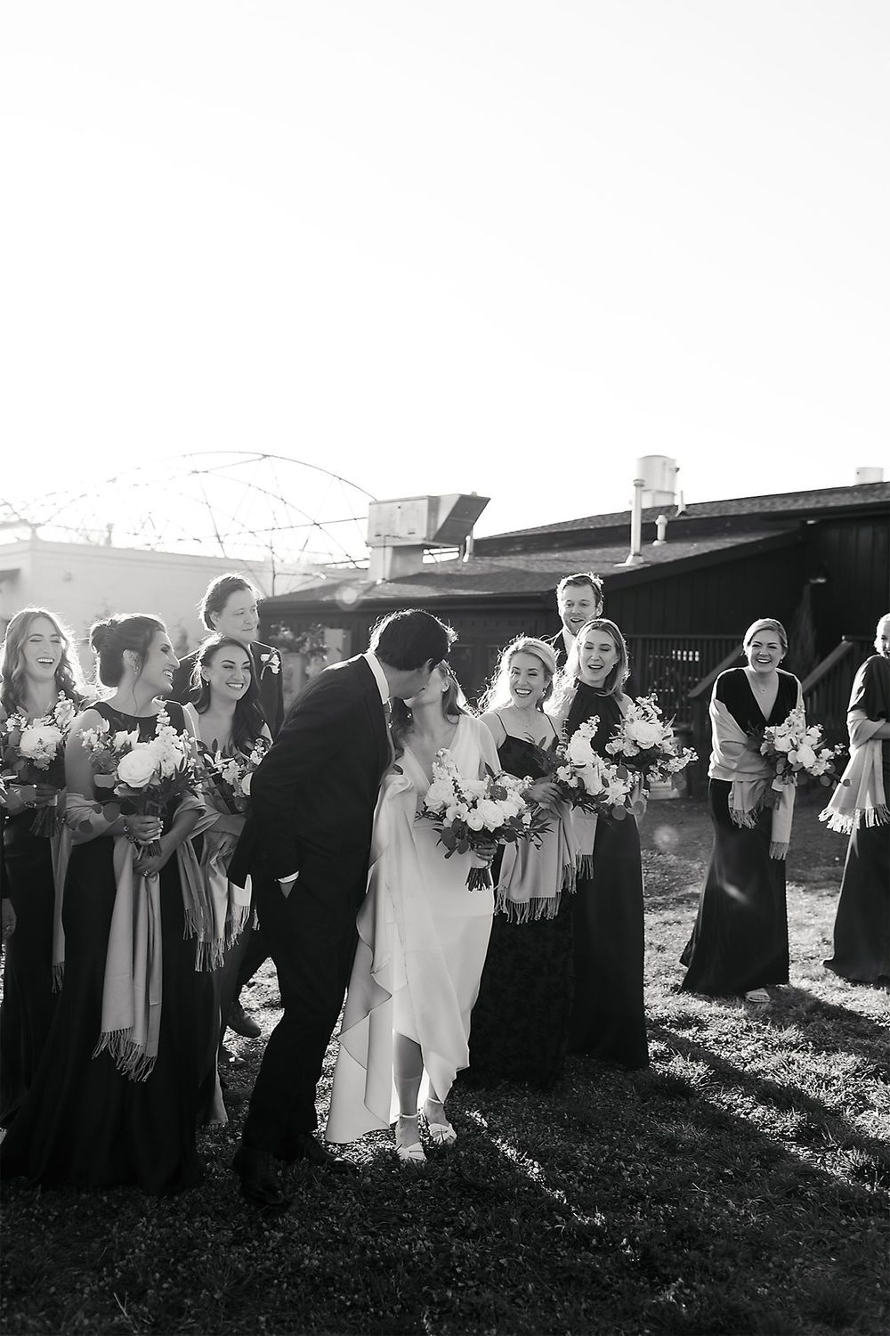 Black and white photo of a wedding party gathered outdoors with bridesmaids holding bouquets.