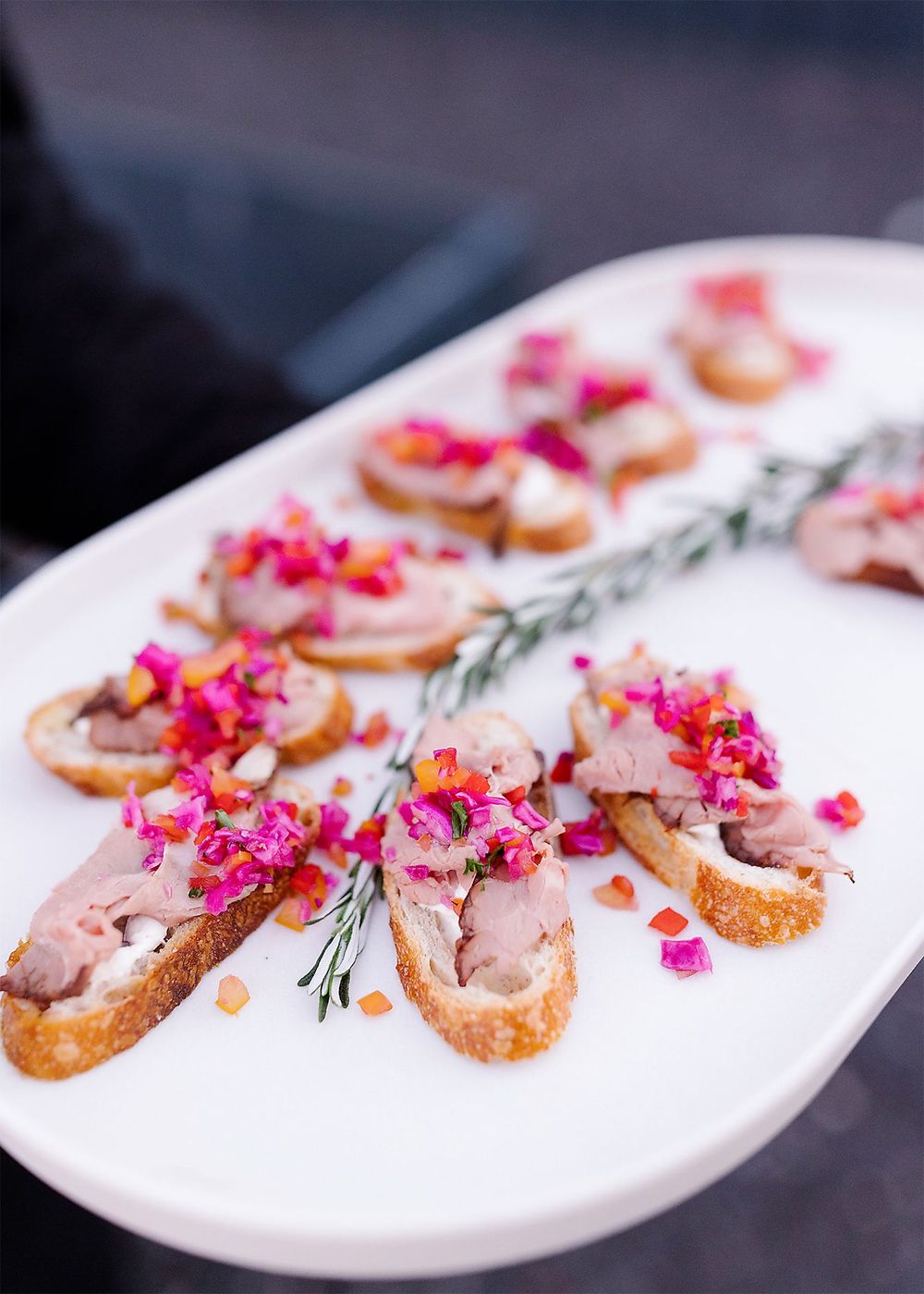 Elegant crostini appetizers topped with pate and vibrant pink flower petals arranged on a white serving platter.