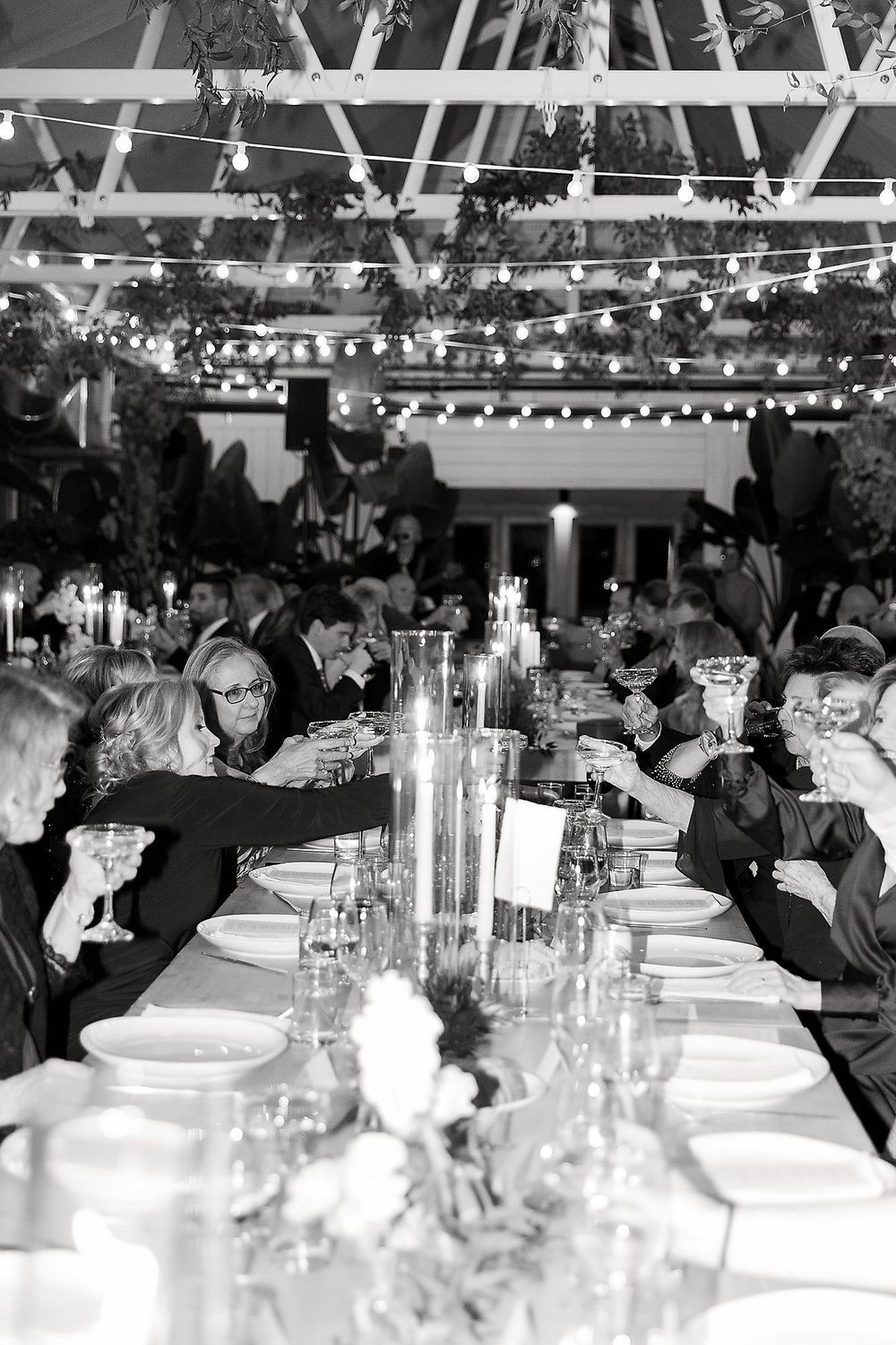 Wedding reception table setup with string lights overhead and guests dining in an elegant black and white setting.