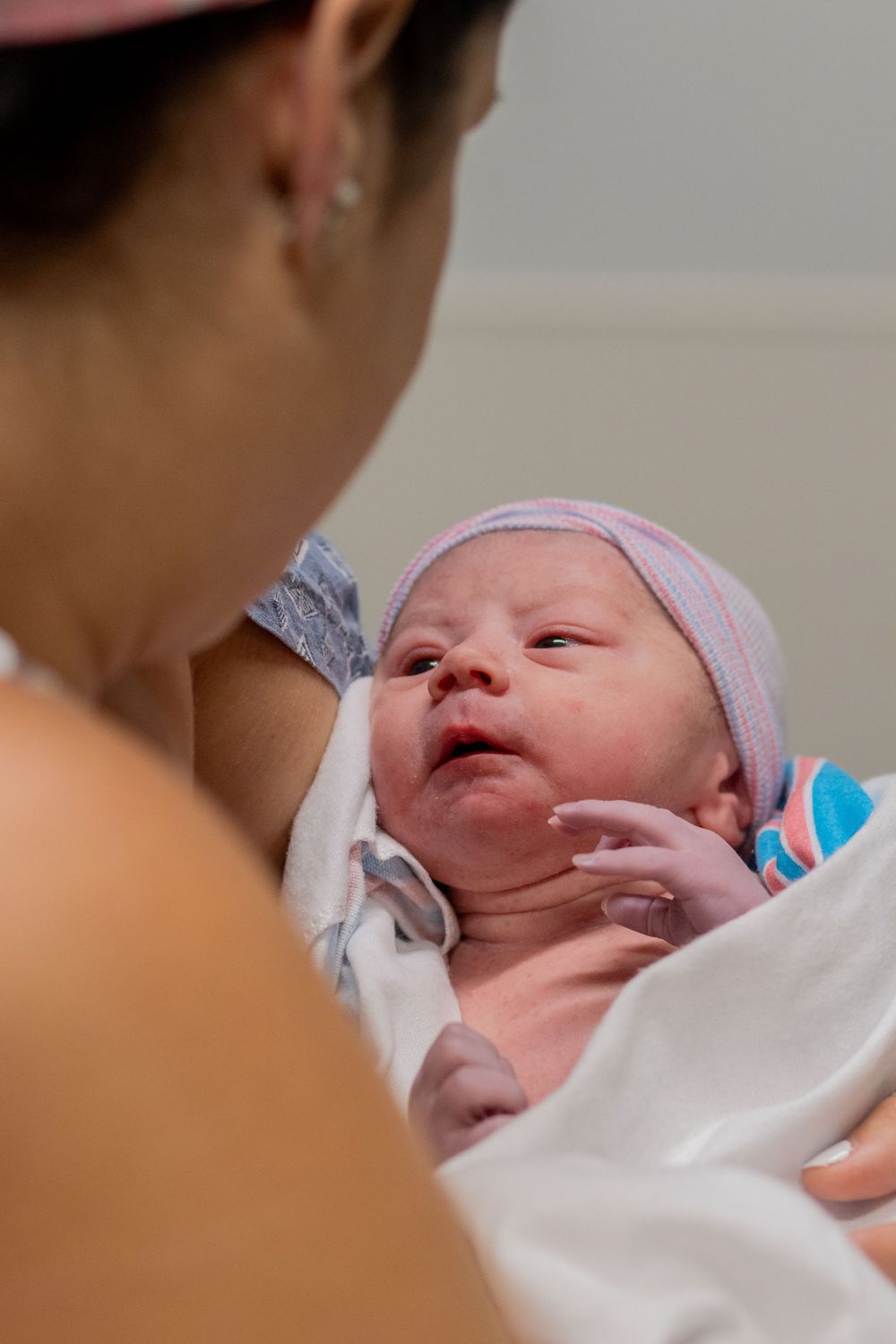 A newborn baby wearing a pink cap lies swaddled in white hospital blankets.