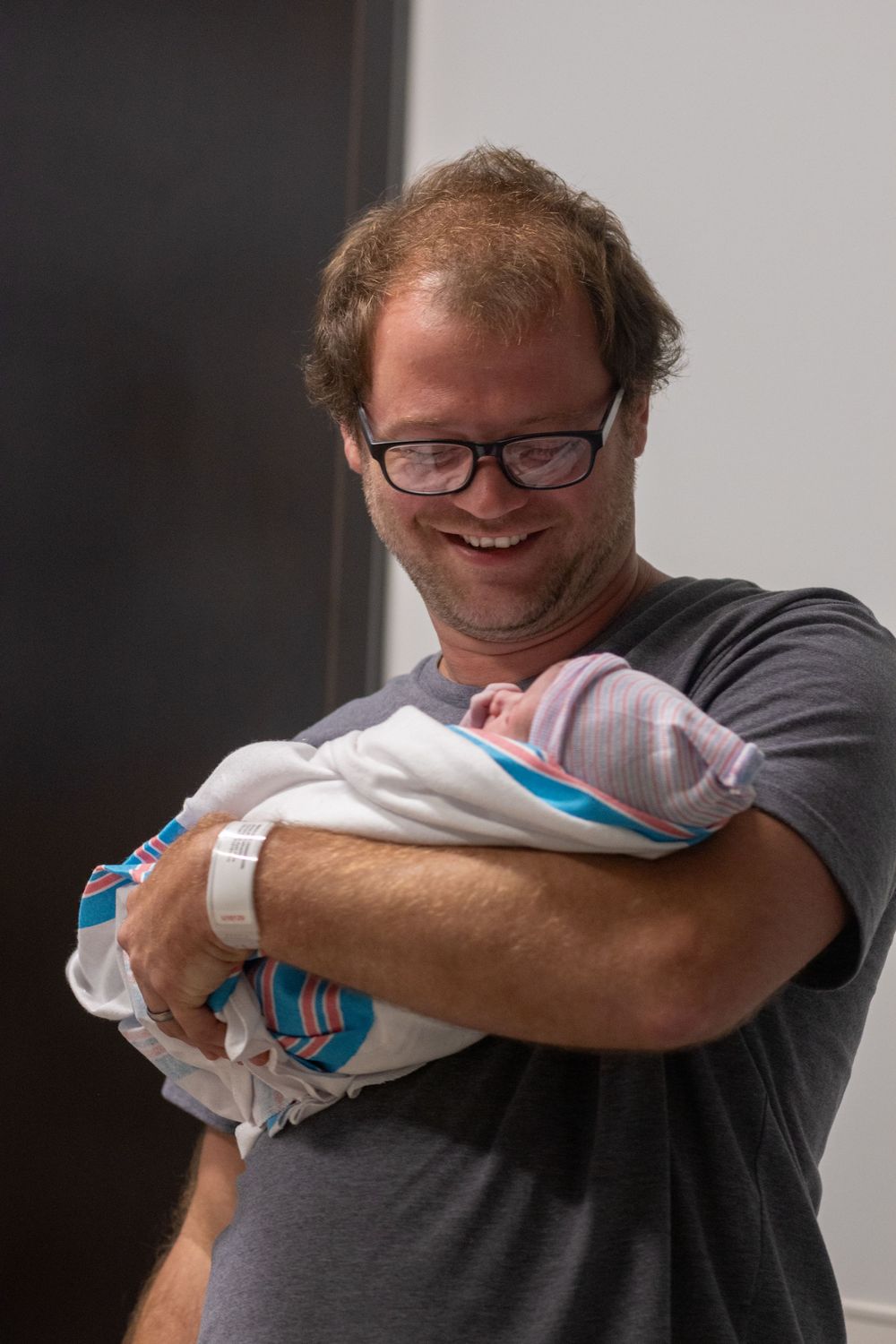 A person in a grey shirt holds and gazes at a swaddled newborn.