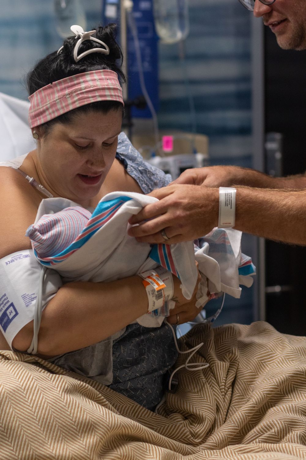 Adults lean over a hospital bed while caring for a newborn baby.