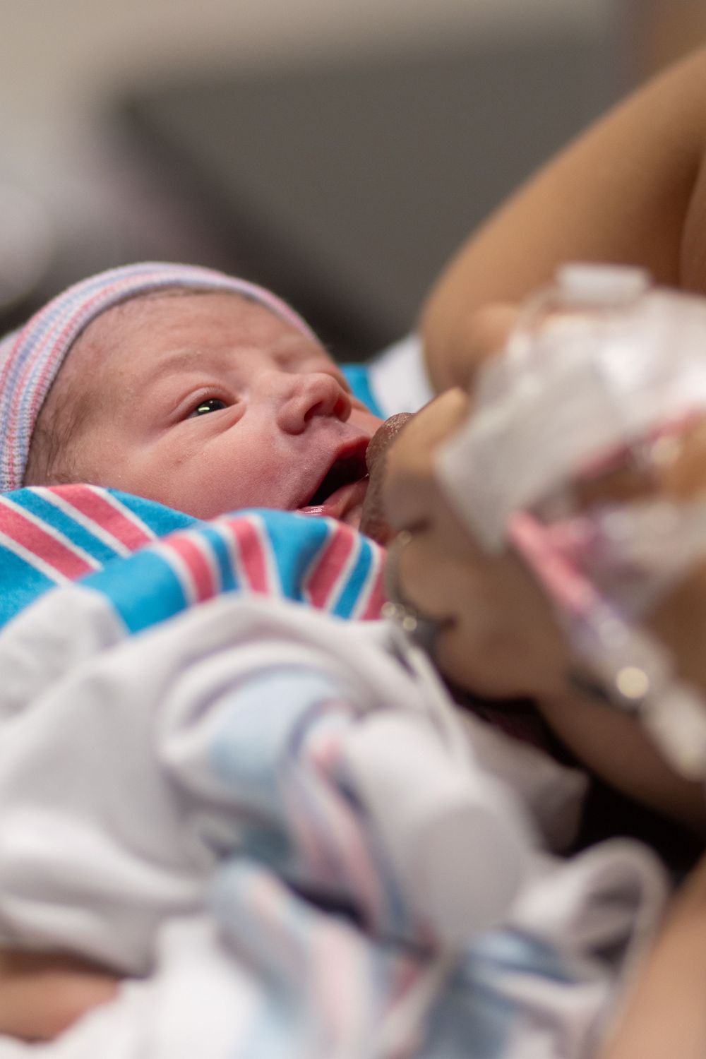 A newborn baby in pink and blue hospital attire rests while being cared for.