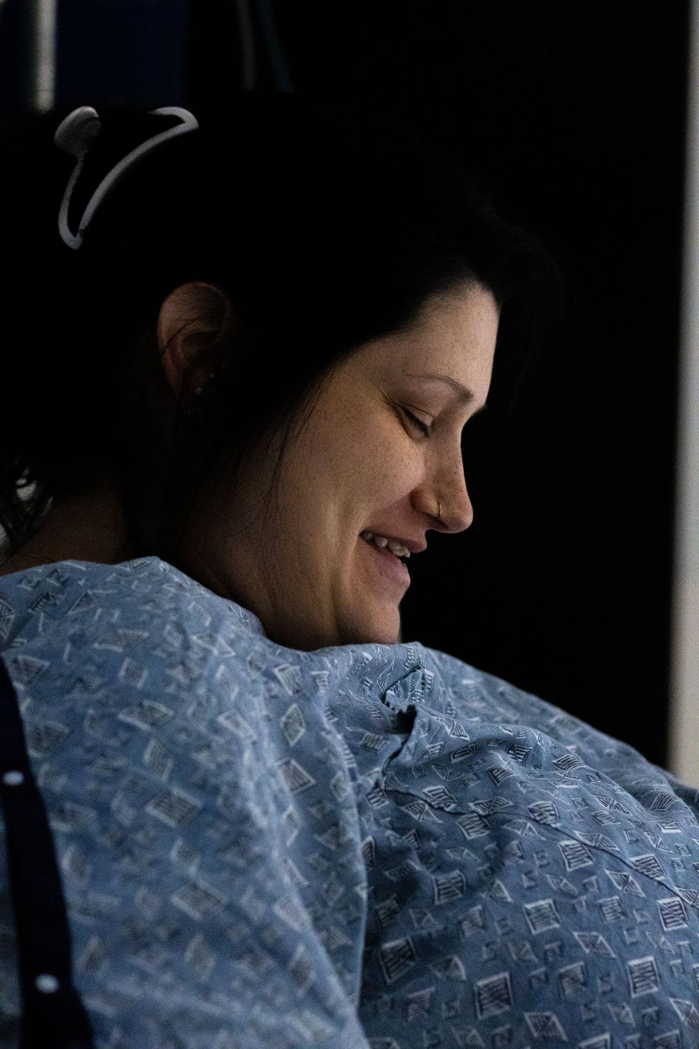 Person wearing a blue hospital gown smiles while resting in a medical setting.