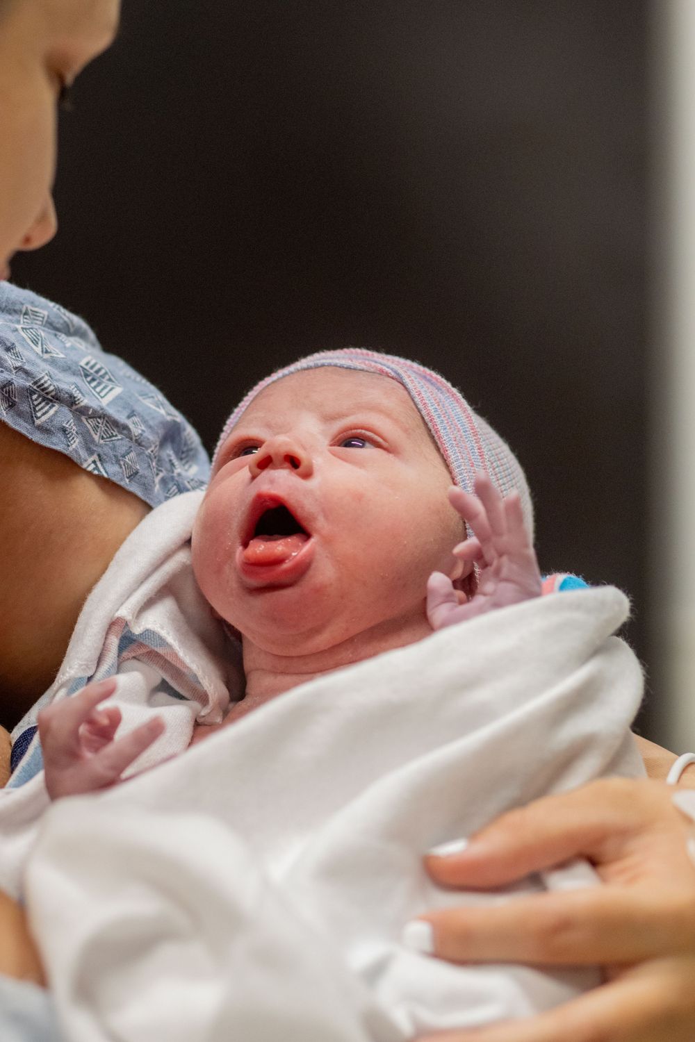 Newborn baby wrapped in white blanket crying shortly after birth.