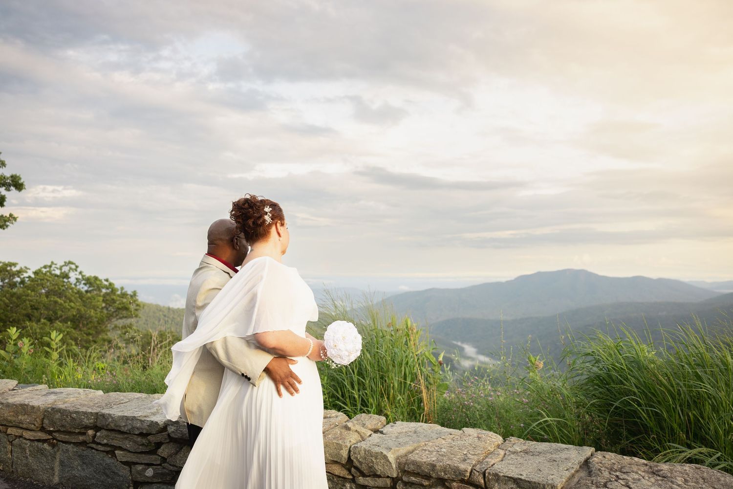 A romantic mountain overlook with rolling hills and scenic vistas provides the backdrop for an intimate wedding moment.