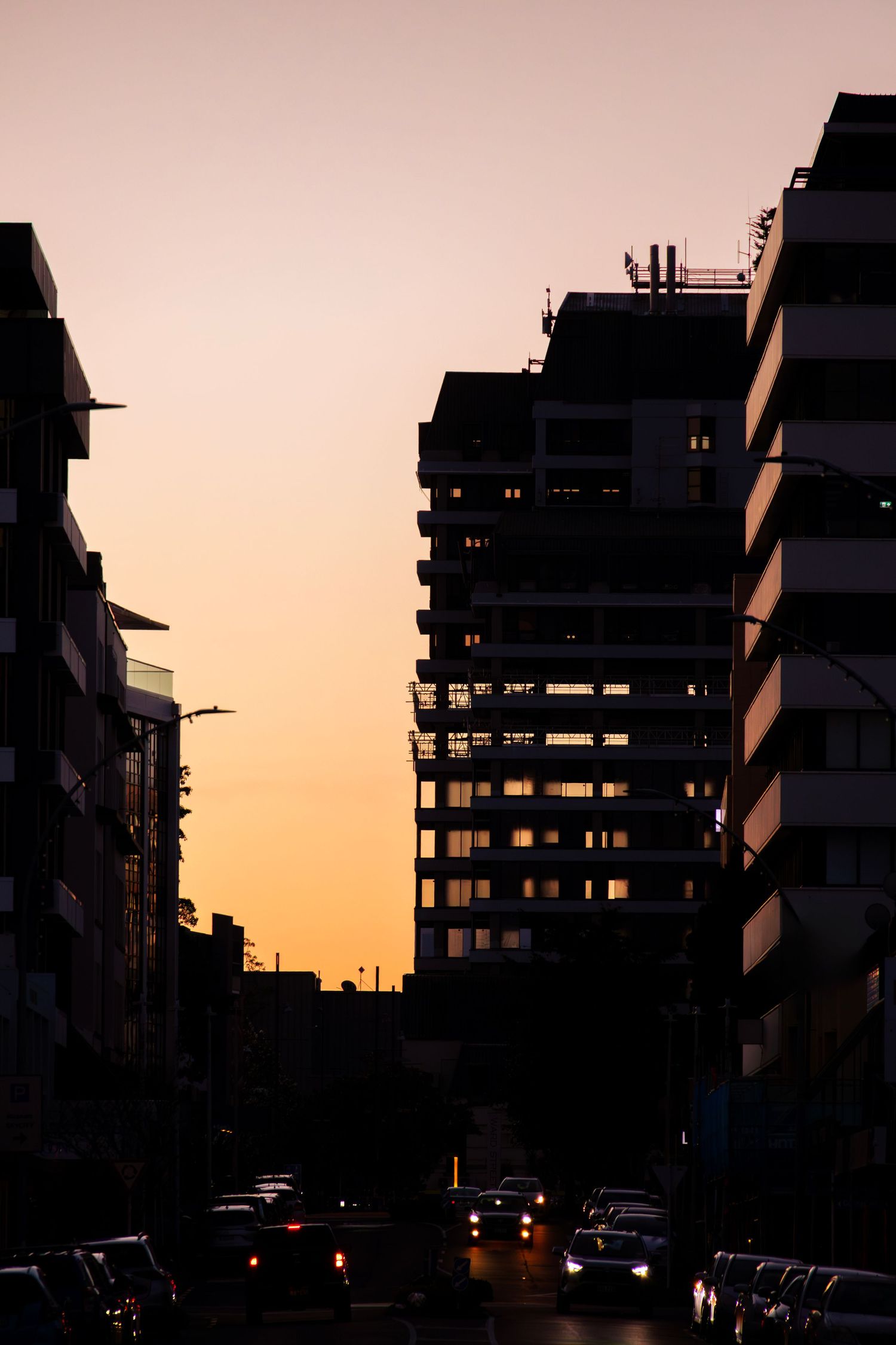 Silhouetted high-rise buildings and street traffic set against a softly fading orange and purple evening sky.