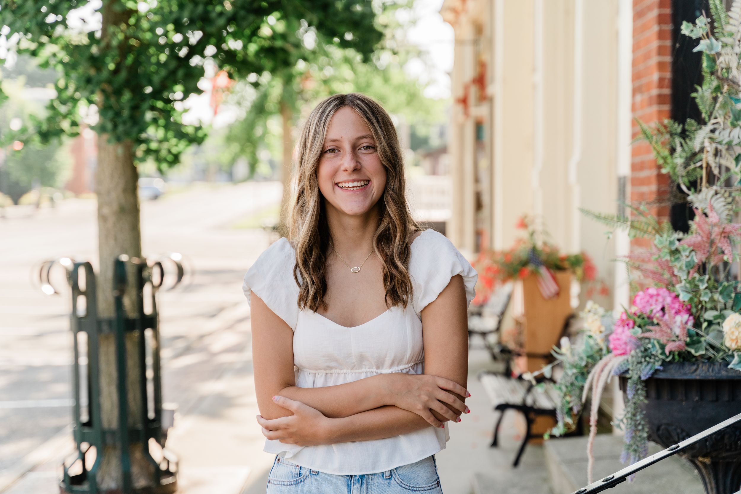 A casual outdoor portrait on a brick-lined sidewalk with potted flowers and greenery in the background.