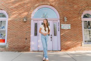 A girl in jeans looks up at pink lockers against a brick wall with sunlight casting diagonal shadows.