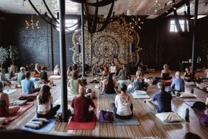 Yoga class participants seated on mats in front of large mandala wall art in modern studio space.