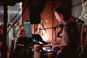 Musician performing with electronic equipment in a atmospheric brick-walled venue.