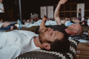 Group relaxation session showing people lying on floor mats in large room.