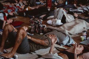 Group meditation session participants lying on floor with meditation cushions.