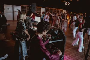Musicians perform with keyboard and instruments while people dance in the background.