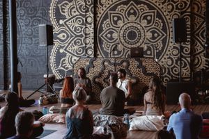 Group meditating in yoga studio with ornate black and white mandala wall mural.