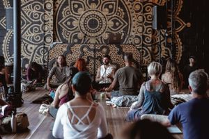 Group meditation session in front of an ornate mandala wall design.