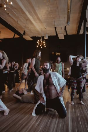 People dancing energetically on a wooden floor under industrial ceiling lights.