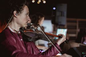 A musician playing violin during a performance in a dark venue.