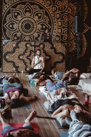 Meditation class participants lying on mats while instructor guides session against decorative wall.