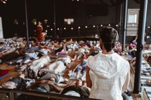 Instructor overlooking a large group meditation session in a studio space.