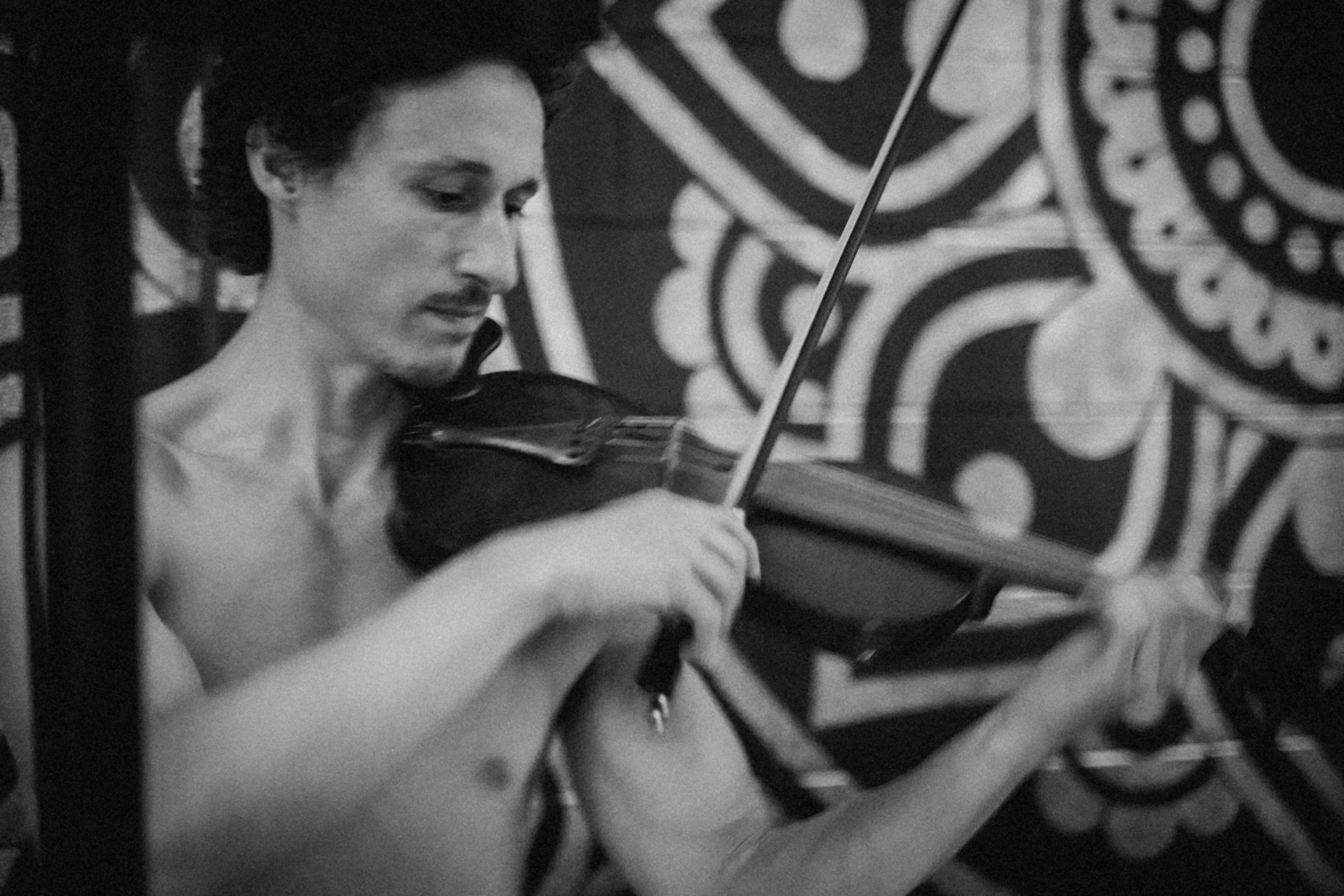 Black and white photo of musician playing violin against decorative patterned backdrop.