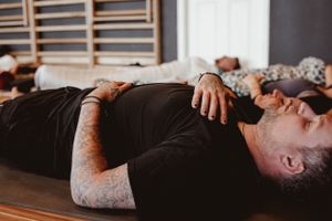 Person lying on back during meditation practice with tattoos visible on arm.