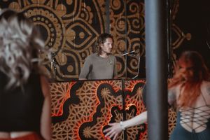 A DJ performing in front of an ornately decorated wall with geometric patterns lit in orange.
