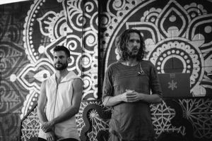 Two people stand against an ornate mandala wall mural in black and white.