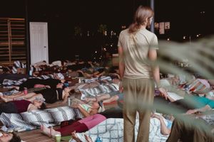 Wellness class participants lying on yoga mats in dimly lit studio space.