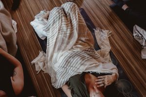 Striped fabric draped over person during relaxation session on wooden floor.