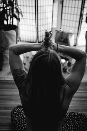 Back view of a person with tattoos sitting in meditation pose with hands clasped behind head.
