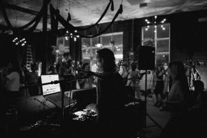 Dark concert venue with silhouetted figure at control board and hanging decorations.