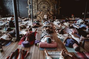 Aerial view of meditation participants lying on mats in a dimly lit studio with mandala wall art.